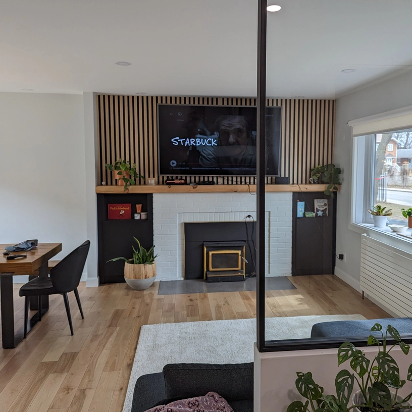 Salon rénové avec foyer blanc, mur décoratif en bois et télévision murale